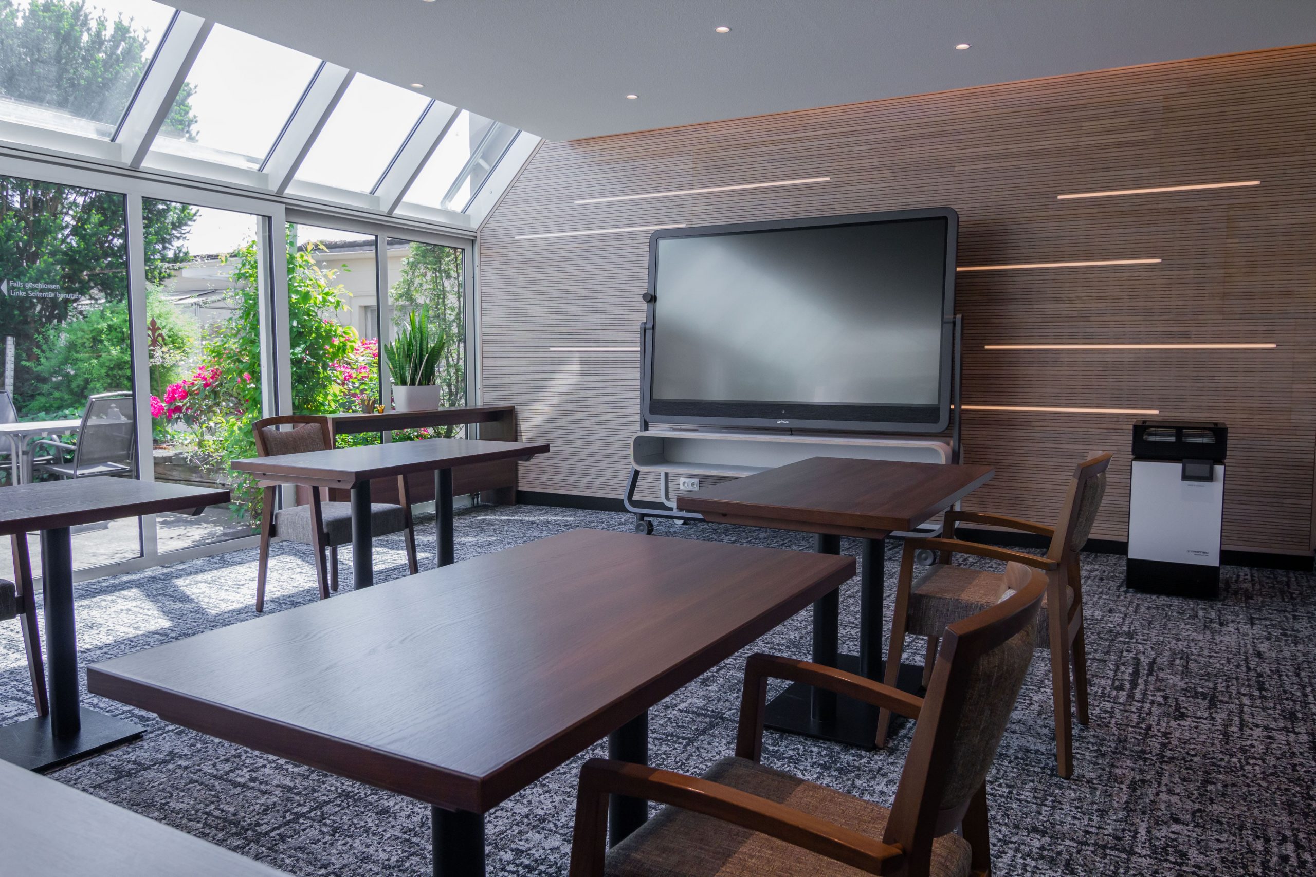 Zoom in den Tagungsraum 3 mit Tischen, Stühlen und Multitouch-Display und Blick auf Terrasse