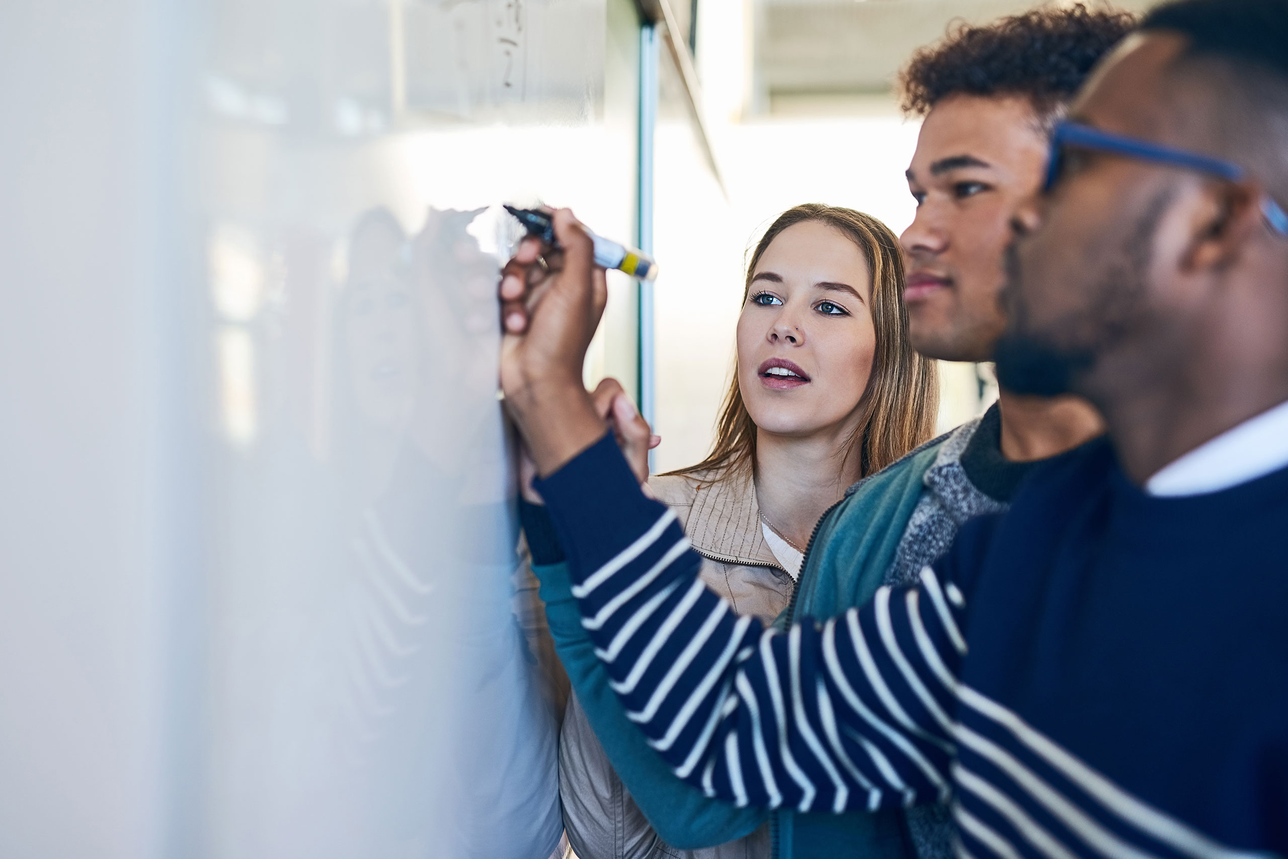 Drei junge Menschen stehen vor einem Whiteboard